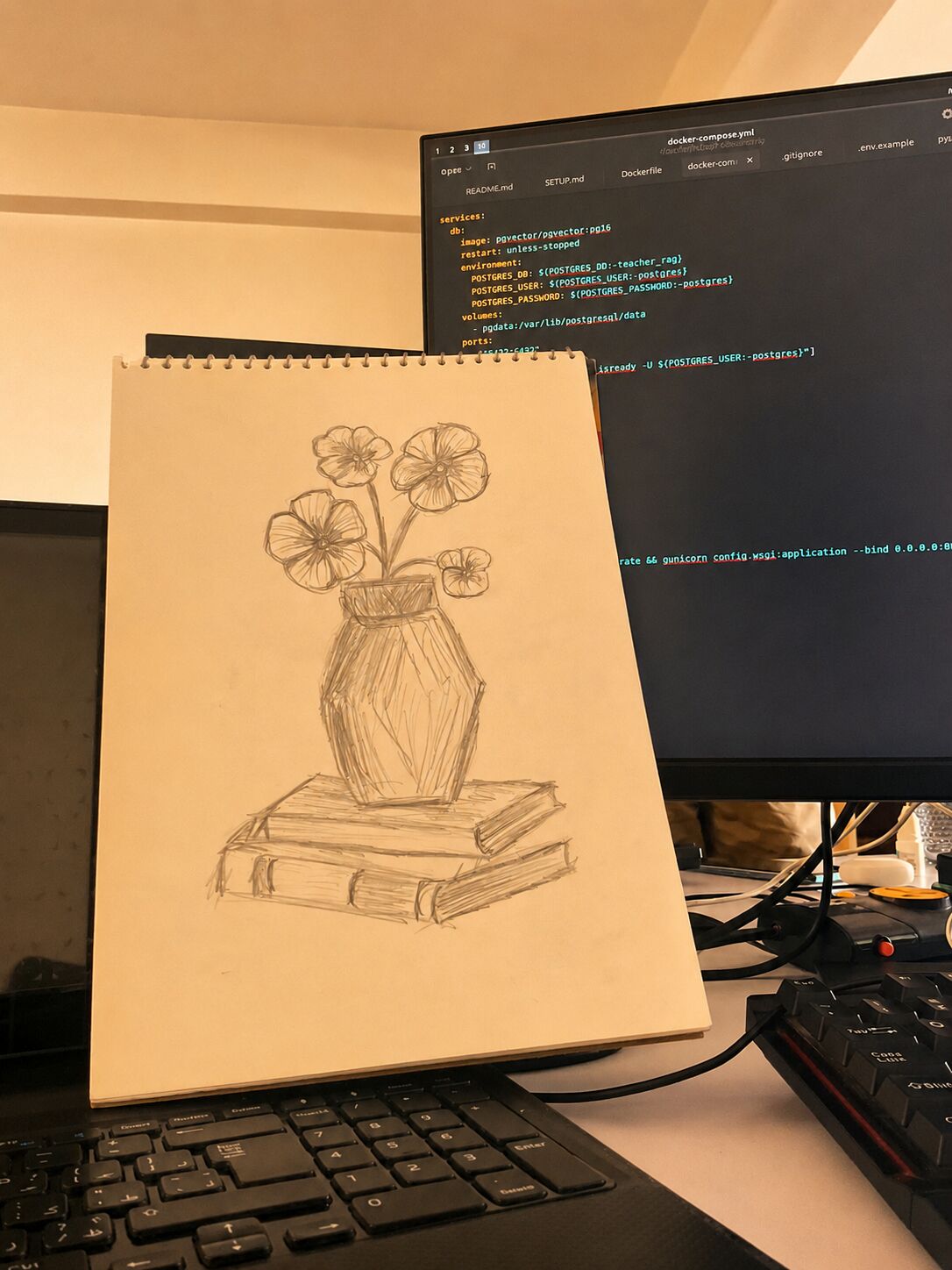 Pencil drawing of flowers in a vase on stacked books, beside a code terminal