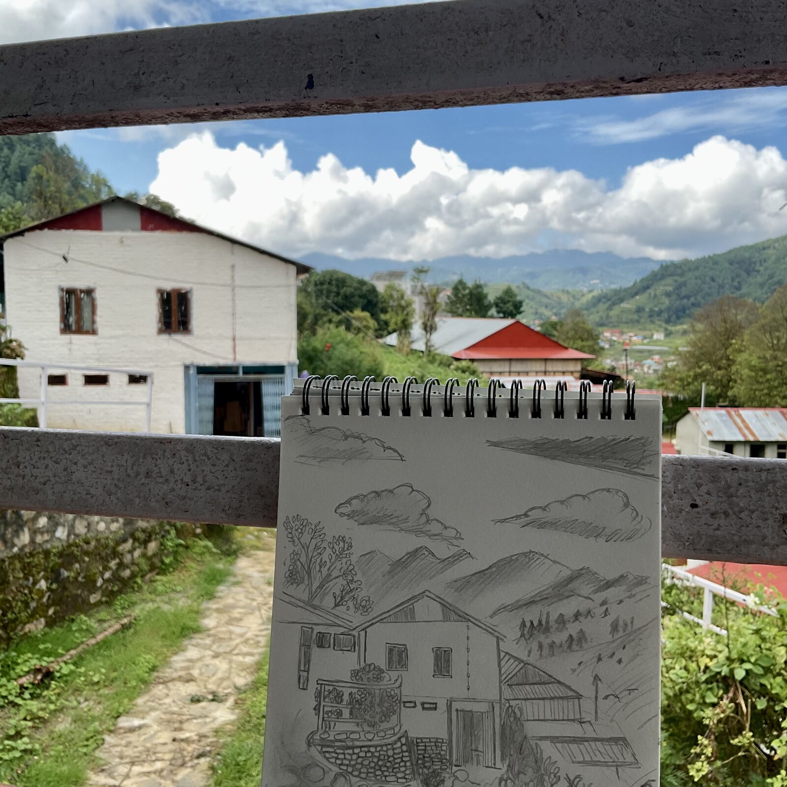 Pencil drawing of a resort held up in front of the real view