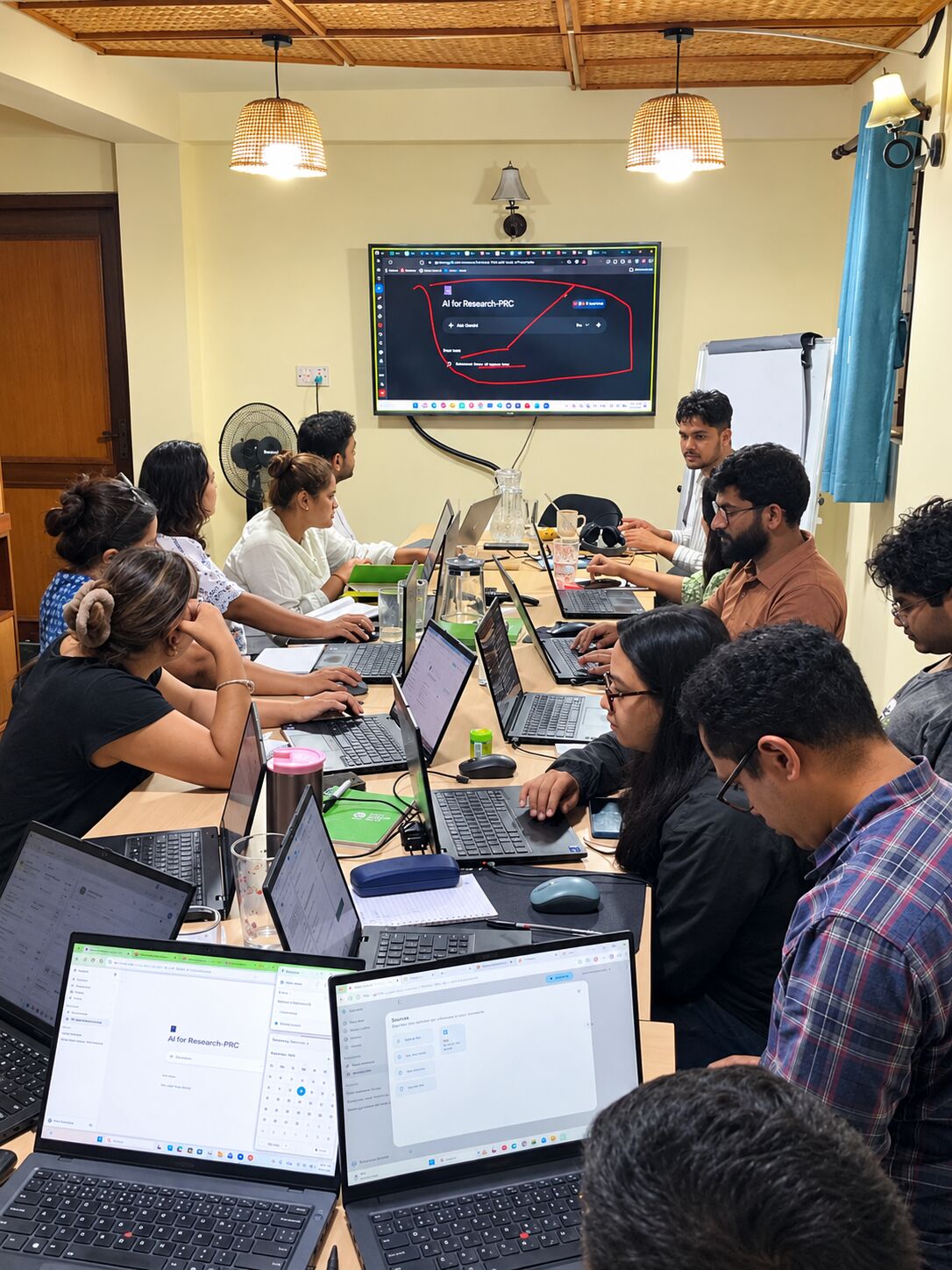 Researchers at a long table with laptops during the AI for Research training at Prakriti Resource Centre