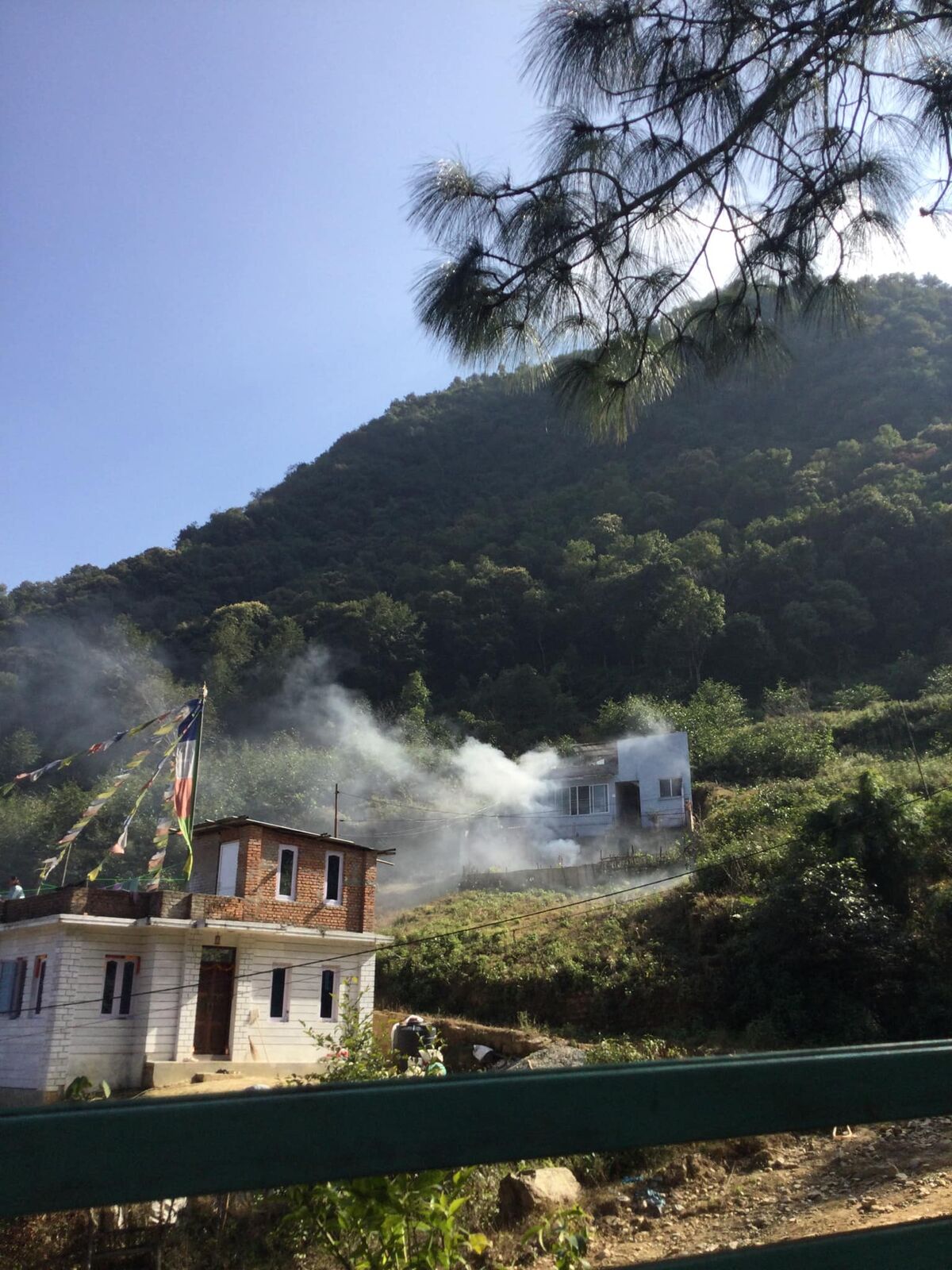 Hillside house with prayer flags and rising smoke